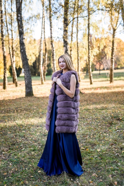 Mujer de moda. Niña sonriente en posin de abrigo de piel en otoño parque con árboles y hiedra