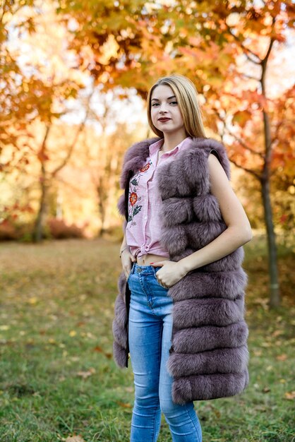 Mujer de moda. Niña sonriente en posin de abrigo de piel en otoño parque con árboles y hiedra