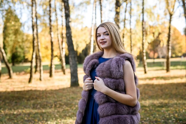 Mujer de moda. Niña sonriente en posin de abrigo de piel en otoño parque con árboles y hiedra