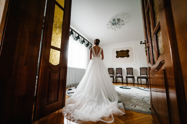 Mujer de moda perfecta modelo con peinado en casa. Hermoso estilo de novia. Chica de boda retrocede en vestido de novia de lujo junto a la ventana.