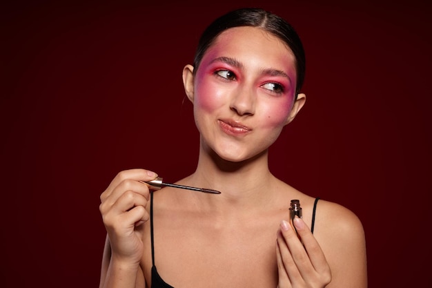 Mujer de moda Pincel de maquillaje cuero limpio maquillaje brillante posando fondo rosa inalterado