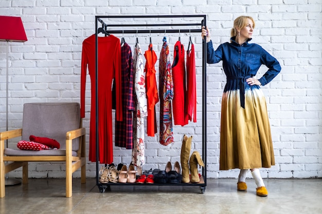 Mujer de moda posando con perchero lleno de zapatos y accesorios de ropa de moda en loft studio