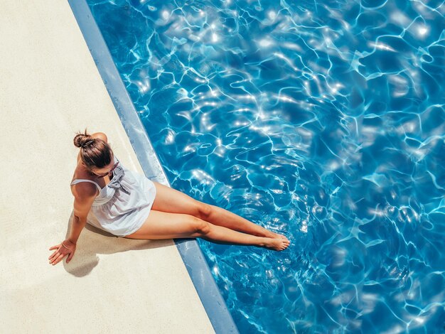 Mujer de moda sentada junto a la piscina en la cubierta vacía