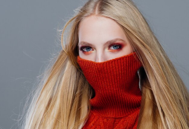 Mujer de moda suéter de punto con cabello largo rubio otoño elegante sobre pared gris