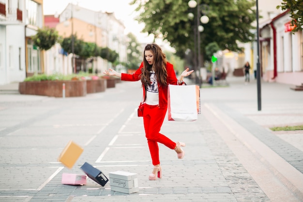 La mujer de moda en traje rojo con bolsas de compras dejó caer cajas de zapatos en la calle.