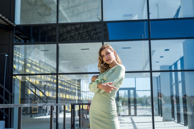 Mujer de moda en vestido verde cerca del edificio moderno de cristal. elegante retrato femenino