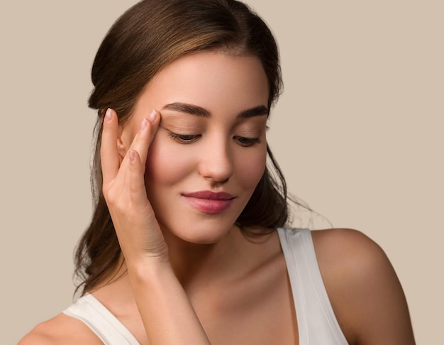 Mujer modelo de belleza con maquillaje natural saludable piel limpia tocando su cara Fondo de color marrón