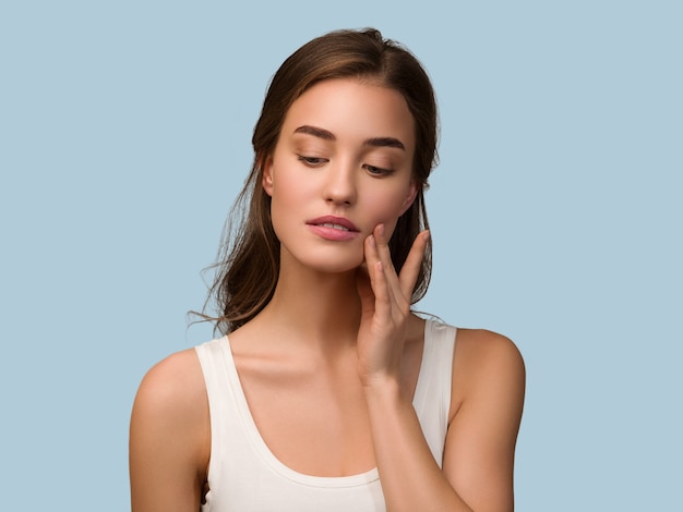 Mujer de modelo de belleza con maquillaje natural saludable piel limpia tocando su rostro Color de fondo azul