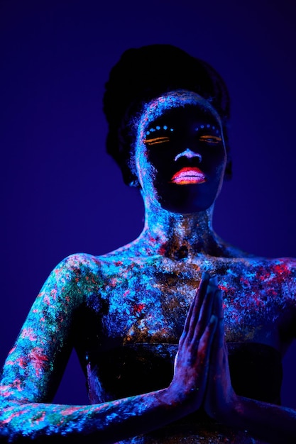 Mujer modelo de moda negra en modelo de luz de neón con maquillaje fluorescente en diseño de arte de posición de oración ...