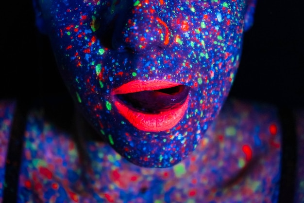 Mujer modelo de moda en retrato de luz de neón de una hermosa modelo con diseño de arte corporal de maquillaje fluorescente en maquillaje colorido de cara pintada UV sobre un fondo negro de una niña Bailarina de discoteca en luz de neón