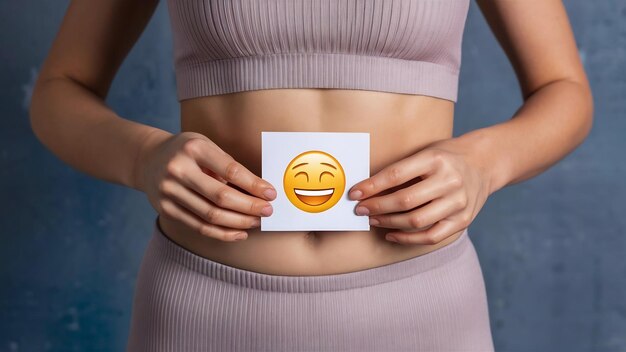 Foto mujer modelo de salud femenina sosteniendo una tarjeta con emoji cerca del estómago