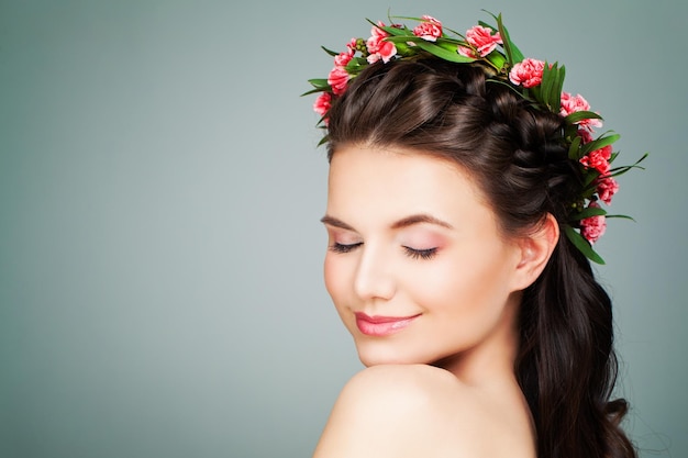 Mujer modelo de spa saludable relajante sobre fondo azul. Chica de spa con maquillaje nude natural, cabello ondulado y corona de flores de verano