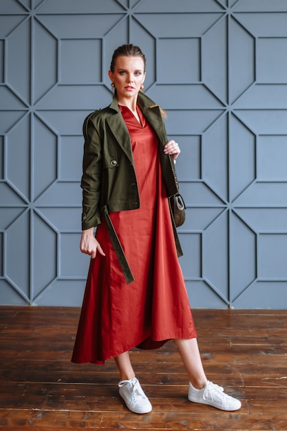 Una mujer modelo con un vestido rojo, una chaqueta verde y un bolso. Demostración de ropa para el showroom.