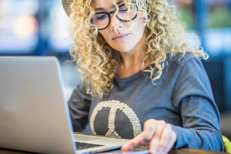 Foto mujer moderna adulta joven que trabaja en la mesa de la tienda con computadora portátil y teléfono móvil en conexión de roaming trabajo nómada digital en línea en la oficina de viajes trabajadora remota mujeres con anteojos