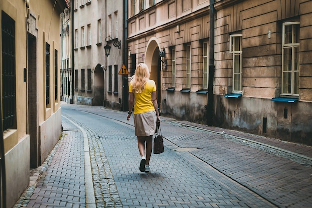 Mujer moderna con camiseta amarilla, caminando por las antiguas calles de Varsovia