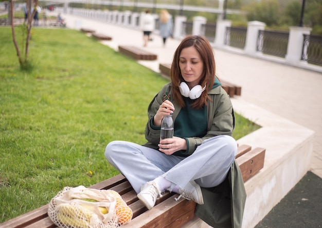 una mujer moderna está sentada en el banco de la calle y va a beber agua