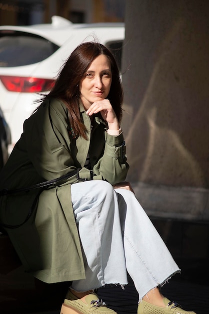 una mujer moderna está sentada en el banco de la calle y sonriendo