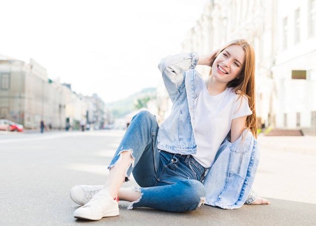 Foto mujer moderna joven elegante que se sienta en el camino y la presentación