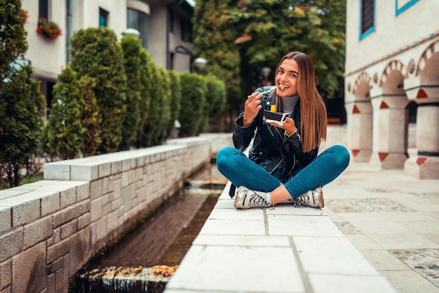 Una mujer moderna se sienta en el parque en un descanso de la universidad y come poffertjes frescos. Enfoque selectivo. foto de alta calidad