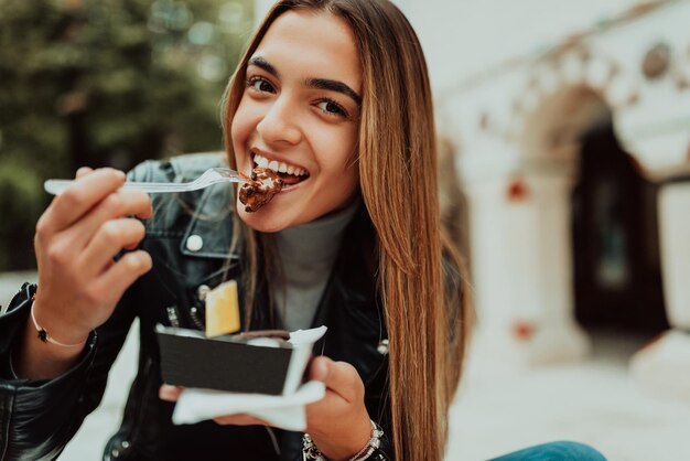 Una mujer moderna se sienta en el parque en un descanso de la universidad y come poffertjes frescos Enfoque selectivo