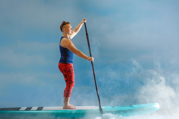 Una mujer con un mohawk en una tabla de snowboard en la niebla contra el fondo de las nubes