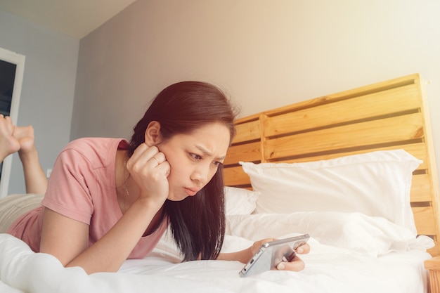 Mujer molesta está jugando juego de móvil en su cama.