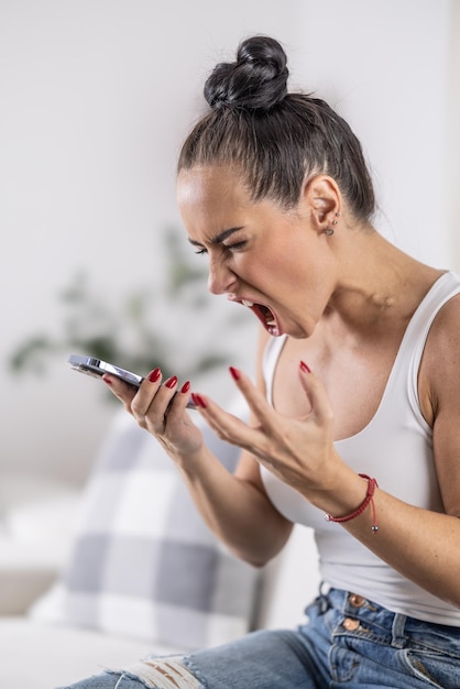 Mujer molesta grita con la boca abierta en el teléfono en el altavoz mostrando un fuerte gesto con la mano