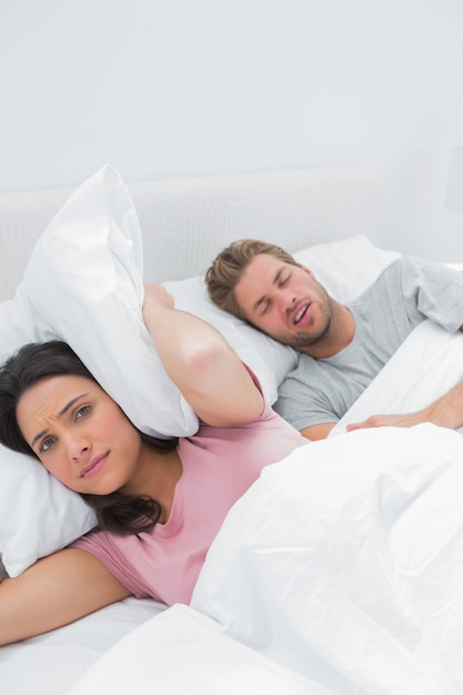 Mujer molesta que cubre las orejas con una almohada junto al marido que ronca