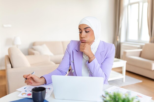 Mujer molesta usando hiyab frente a la búsqueda de computadoras portátiles y haciendo trabajo de oficina finanzas comerciales y concepto de estación de trabajo Empresaria árabe trabajando en casa