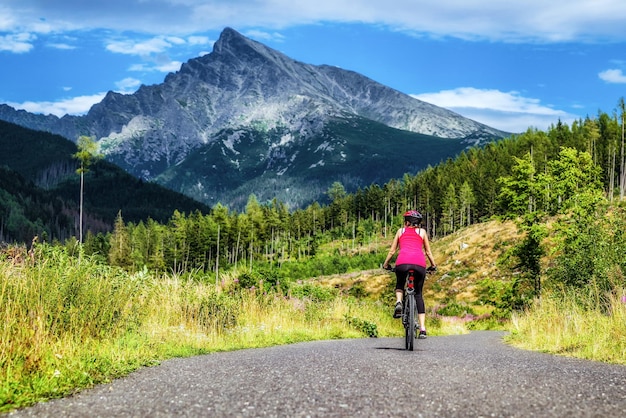 Mujer montando bicicleta de montaña en la carretera en el bosque con colinas al fondo en las montañas High Tatras Eslovaquia