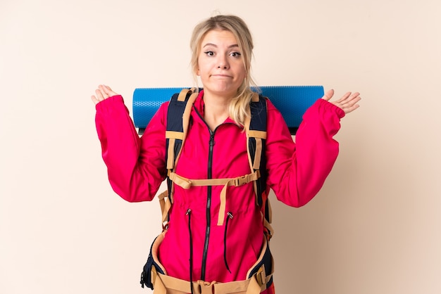 Mujer montañista con una mochila grande sobre aislada tener dudas con expresión de la cara confusa