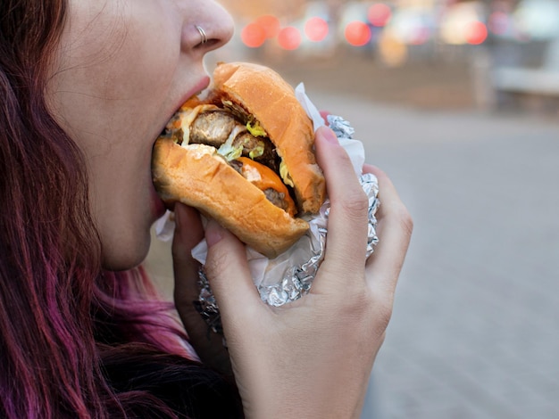 Mujer mordiendo una hamburguesa con 2 chuletas para llevar en la calle de cerca