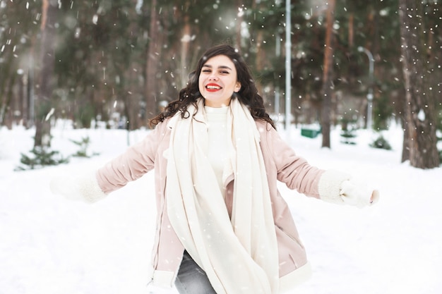 Mujer morena alegre caminando en el bosque en invierno durante las nevadas