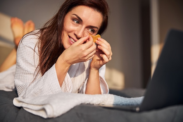 Mujer morena alegre viendo tutoriales de belleza en línea