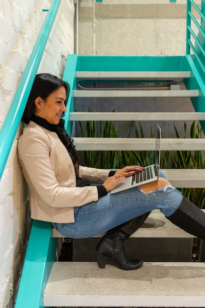 Mujer morena de belleza está trabajando con su computadora portátil desde las escaleras