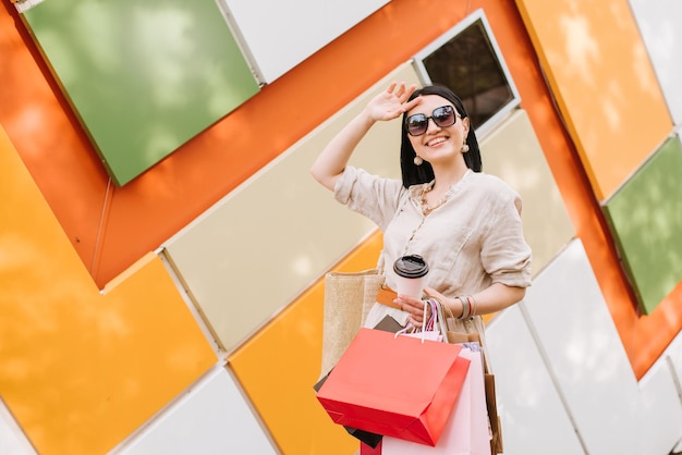 Mujer morena con bolsas de compras posando en la pared de colores de la tienda