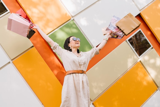 Mujer morena con bolsas de compras posando en la pared de colores de la tienda