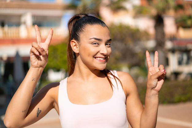 Mujer morena bonita joven que muestra el signo de la victoria con ambas manos