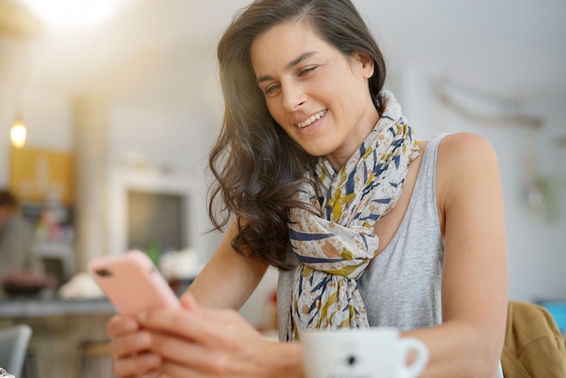 Mujer morena en cafetería con smartphone