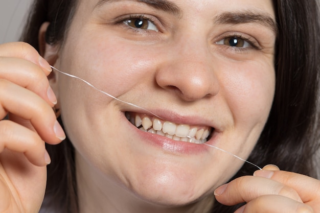 Una mujer morena se cepilla los dientes con hilo dental.