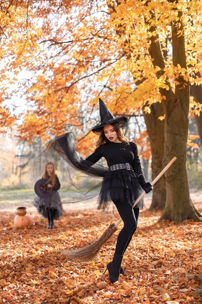 Mujer morena disfrazada de bruja parada en el bosque de otoño el día de Halloween. Mujer con ropa negra y sombrero de cono. Mujer sentada en una escoba.