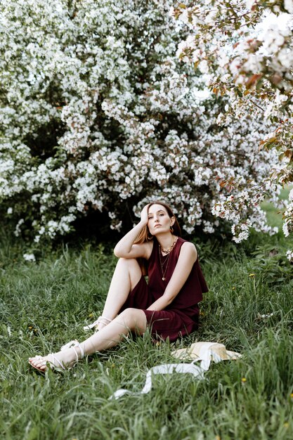 Una mujer morena con un elegante traje se encuentra cerca de los manzanos en flor en un cálido día de verano.