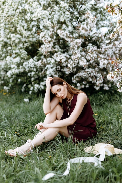 Una mujer morena con un elegante traje se encuentra cerca de los manzanos en flor en un cálido día de verano.