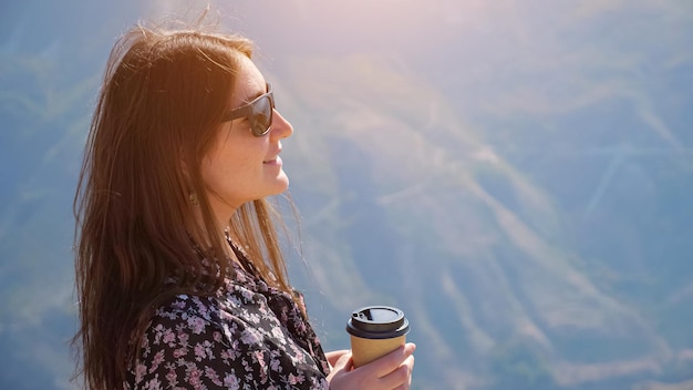 Mujer morena con elegantes gafas de sol en vestido de color bebe café disfrutando del maravilloso paisaje del valle montañoso en Highland en primer plano de día soleado