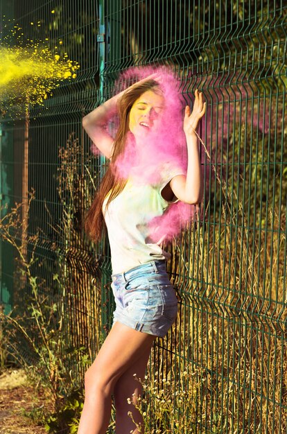 Mujer morena emocional posando con explosión de polvo de Holi rosa y amarillo en el parque