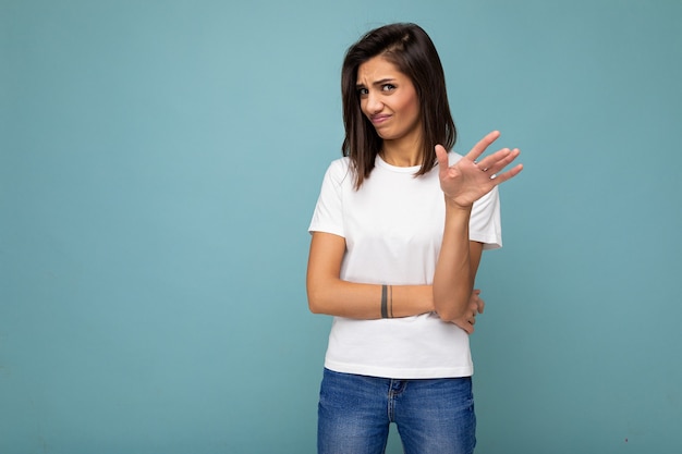 Mujer morena con emociones sinceras vistiendo camiseta blanca casual para maqueta aislado sobre azul