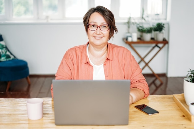 Foto mujer morena encantadora adulta con gafas de cuerpo positivo trabajando con una laptop en la oficina en casa