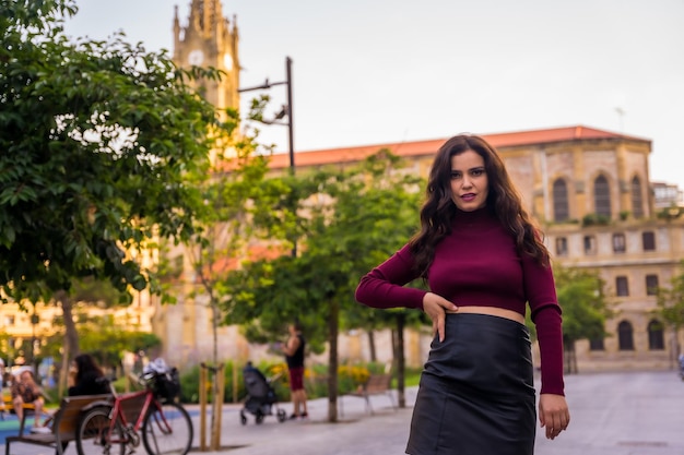 Una mujer morena con falda de cuero junto a una iglesia visitando el estilo de vida de la ciudad