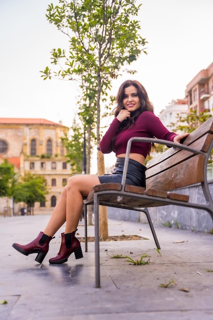 Una mujer morena con falda de cuero sentada en la ciudad con una iglesia al fondo en otoño