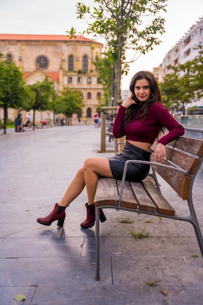 Una mujer morena en una falda de cuero sentada en la pose de moda de estilo de vida de la ciudad foto vertical